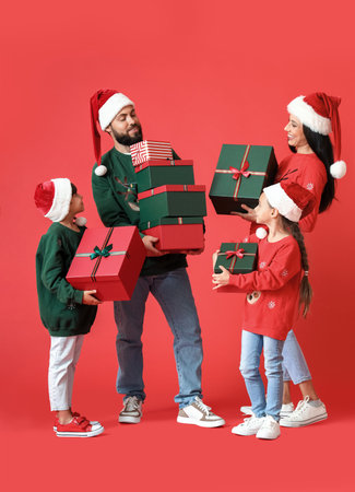 Happy family in Santa hats with Christmas gifts on red backgroundの写真素材