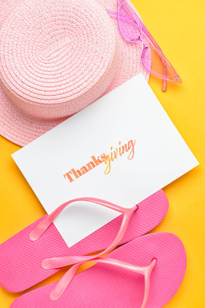 Beach hat, flip flops, eyeglasses and paper card with word THANKSGIVING on color background, closeupの写真素材