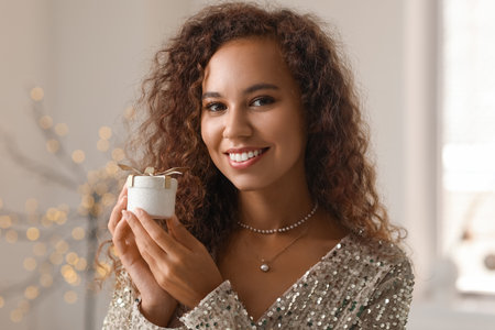 Young African-American woman with small Christmas gift at homeの写真素材