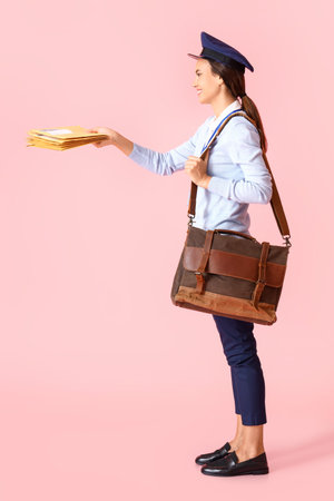 Young postwoman with letters and bag on pink background
