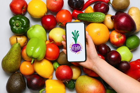 Fresh fruits, vegetables and woman holding mobile phone with text WORLD VEGAN DAY NOVEMBER 1 on gray backgroundの写真素材