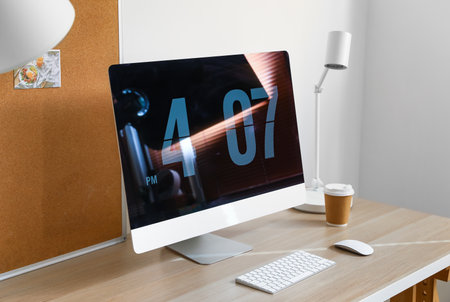 Modern computer with cup of coffee and lamp on desk in office