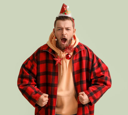 Screaming young man in stylish winter clothes and with Christmas decor on light background