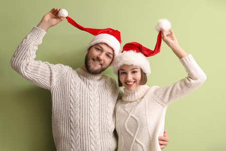 Happy young couple in stylish winter clothes and Santa Claus hats on color backgroundの写真素材