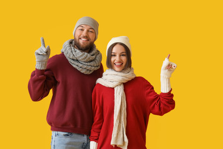 Happy young couple in stylish winter clothes showing something on color backgroundの写真素材