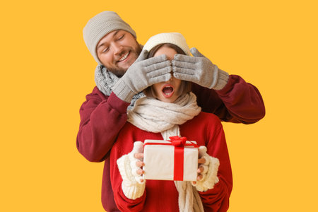 Young woman receiving Christmas gift from her boyfriend on color backgroundの写真素材