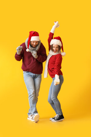 Dancing young couple in stylish winter clothes and Santa Claus hats on color backgroundの写真素材