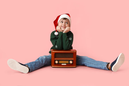 Little boy in Santa hat and with radio receiver listening to Christmas music on color backgroundの写真素材