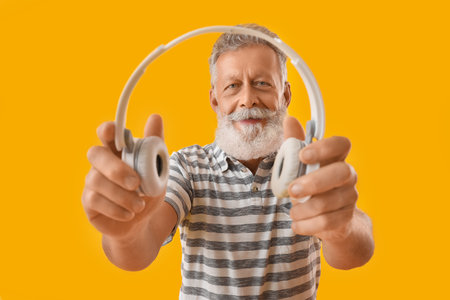 Senior bearded man with headphones on yellow background