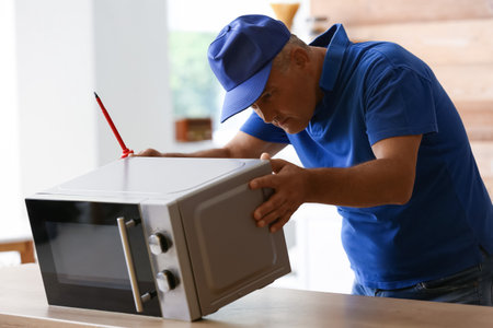 Male worker repairing microwave oven in kitchenの写真素材