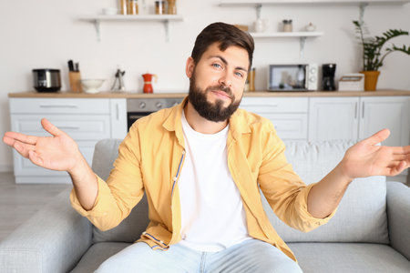 Confused young man video chatting in kitchenの写真素材