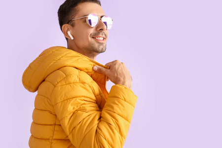 Stylish young man in sunglasses and yellow jacket on lilac background