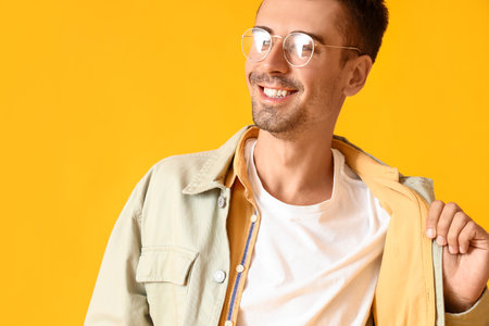 Young man in eyeglasses and stylish jacket on yellow background