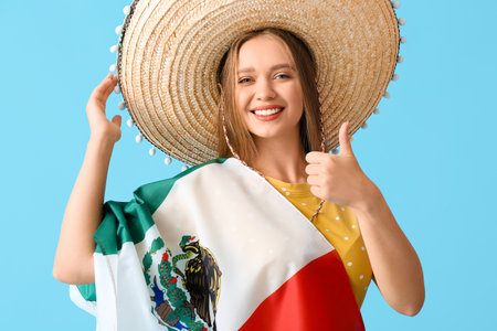 Happy young woman in sombrero hat and with flag of Mexico showing thumb-up gesture on color backgroundの写真素材