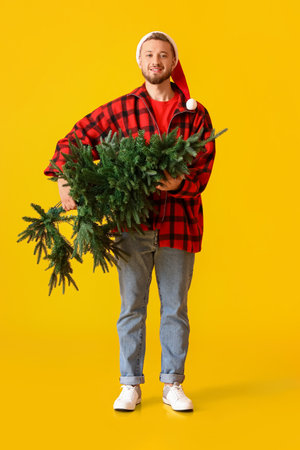 Young man in Santa hat with Christmas tree on yellow backgroundの写真素材