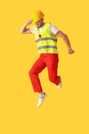 Young male worker jumping on yellow backgroundの写真素材