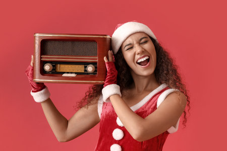 Young African-American woman in Santa hat with retro radio receiver on red backgroundの写真素材