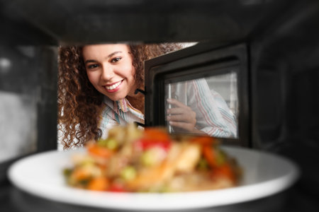 Young African-American woman heating food in microwave oven, view from insideの写真素材