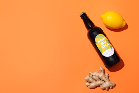 Bottle of fresh kombucha with lemon and ginger on color background