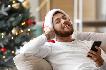 Young man in headphones with mobile phone at home on Christmas eveの写真素材