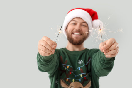 Young man in Santa hat with Christmas sparklers on gray backgroundの写真素材