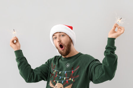 Young man in Santa hat with Christmas sparklers on gray backgroundの写真素材