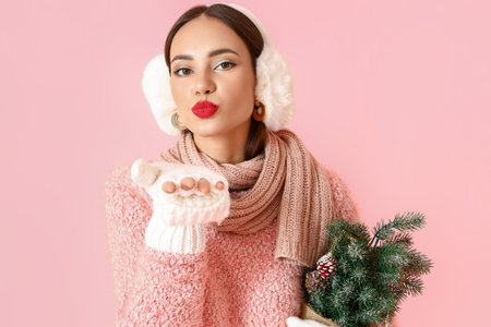 Beautiful woman with small Christmas tree blowing kiss on pink backgroundの写真素材