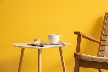 Stylish interior with coffee table and wicker armchair on yellow wall backgroundの写真素材