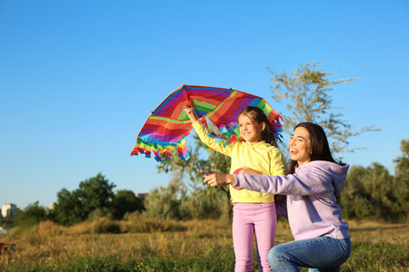 Cute little girl with kite and her mother pointing at something outdoorsの写真素材