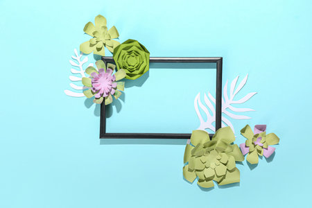 Photo frame with beautiful handmade paper flowers on blue background