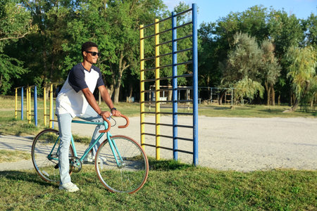 African-American teenage boy in sunglasses with bicycle on sport ground