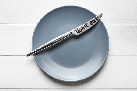 Plate and knife with text DON'T EAT on white wooden background. anorexia concept