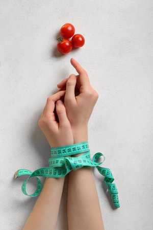 Female hands with measuring tape and tomatoes on light background. anorexia conceptの写真素材
