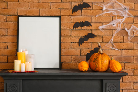 Blank frame with candles and Halloween pumpkins on mantelpiece near brick wallの写真素材