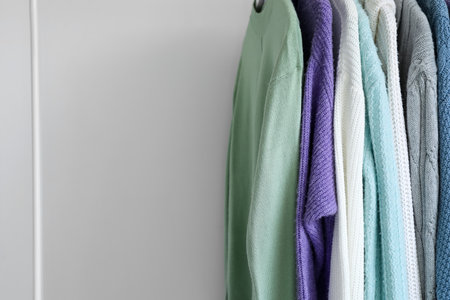 Rack with knitted sweaters near light wall, closeupの写真素材