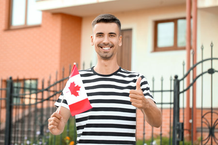 Young man with flag of Canada showing thumb-up outdoorsの写真素材