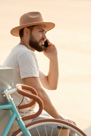 Handsome bearded man with bicycle talking by mobile phone outdoorsの写真素材