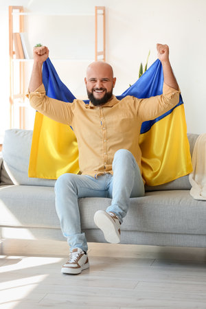 Handsome man with flag of Ukraine sitting on sofa at homeの写真素材
