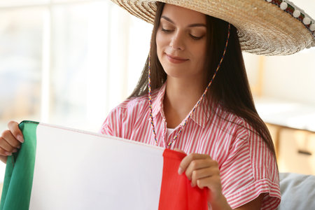 Beautiful young woman in sombrero and with flag of Mexico at homeの写真素材