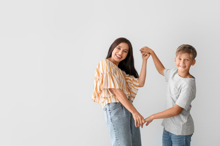 Happy dancing woman and her son on light background