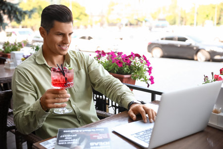 Handsome man with cocktail using laptop at table in street cafeの写真素材
