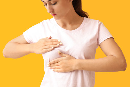 Young woman suffering from breast pain on yellow background, closeupの写真素材