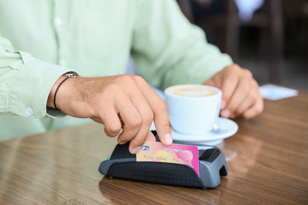 Man paying for coffee with credit card via payment terminal at table in outdoor cafe, closeup