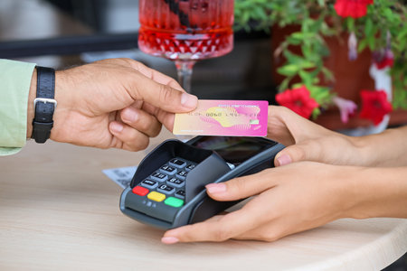 Man paying with credit card via payment terminal at table in cafe, closeup