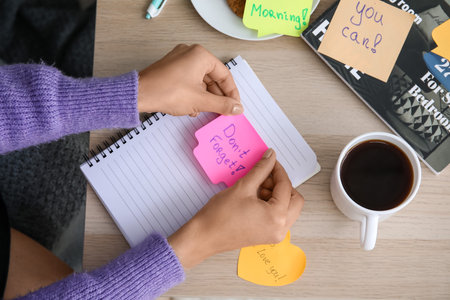 Woman sticking note with text DON'T FORGET on notebook at homeの写真素材