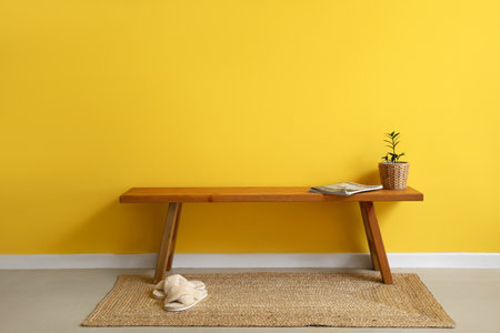 Wooden bench with magazines, flowerpot and slippers near yellow wallの写真素材