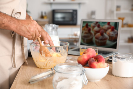 Young man preparing peach muffins while following cooking video tutorial in kitchen, closeup