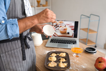 Young man preparing peach muffins while following video tutorial in kitchenの写真素材