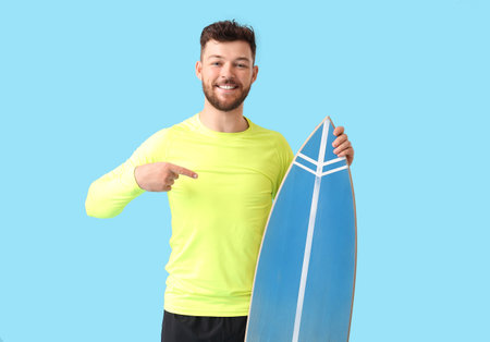 Handsome bearded man pointing at surfboard on blue background