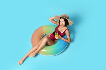 Young woman with cocktail and inflatable ring on color backgroundの写真素材
